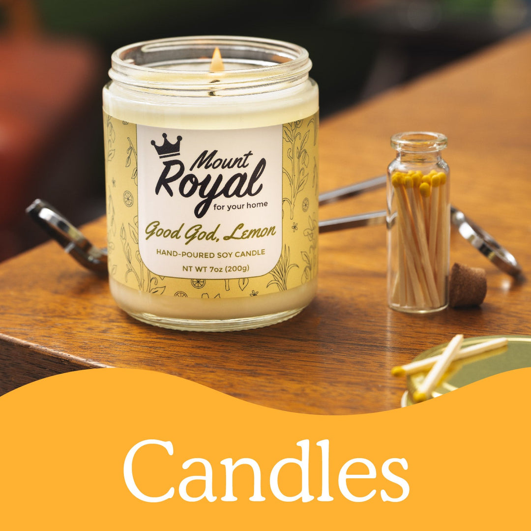 Good god lemon Candle on table lit and burning with a glass bottle of matches and a wick trimmer next to it