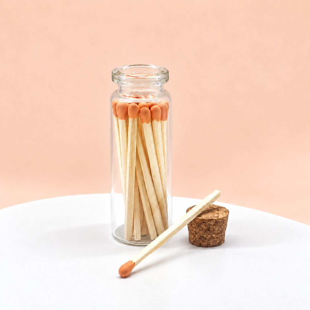Orange matches in a glass jar on a peach background