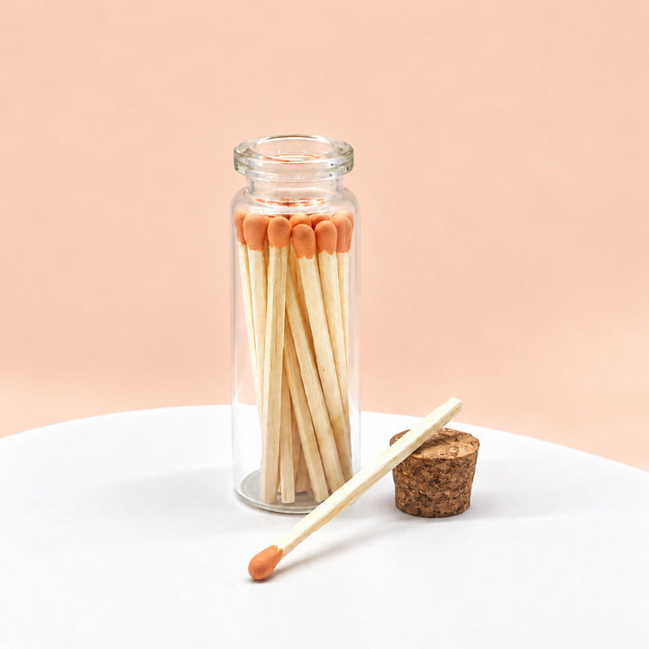 Orange matches in a glass jar on a peach background