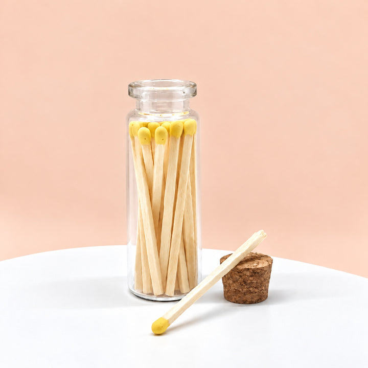 Yellow matches in a glass jar on a peach background