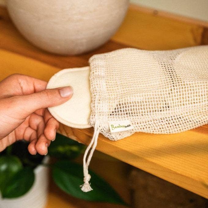A person taking the reusable hemp facial round out of the wash bag made of organic cotton mesh.